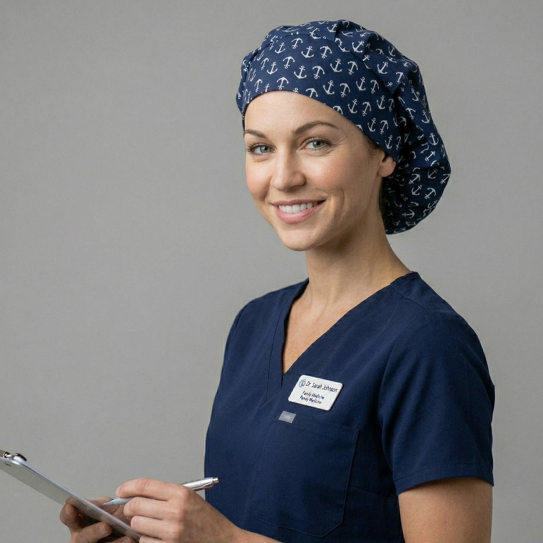 A smiling healthcare professional looking at the camera, holding a tablet and stylus while wearing the anchor-patterned scrub cap.