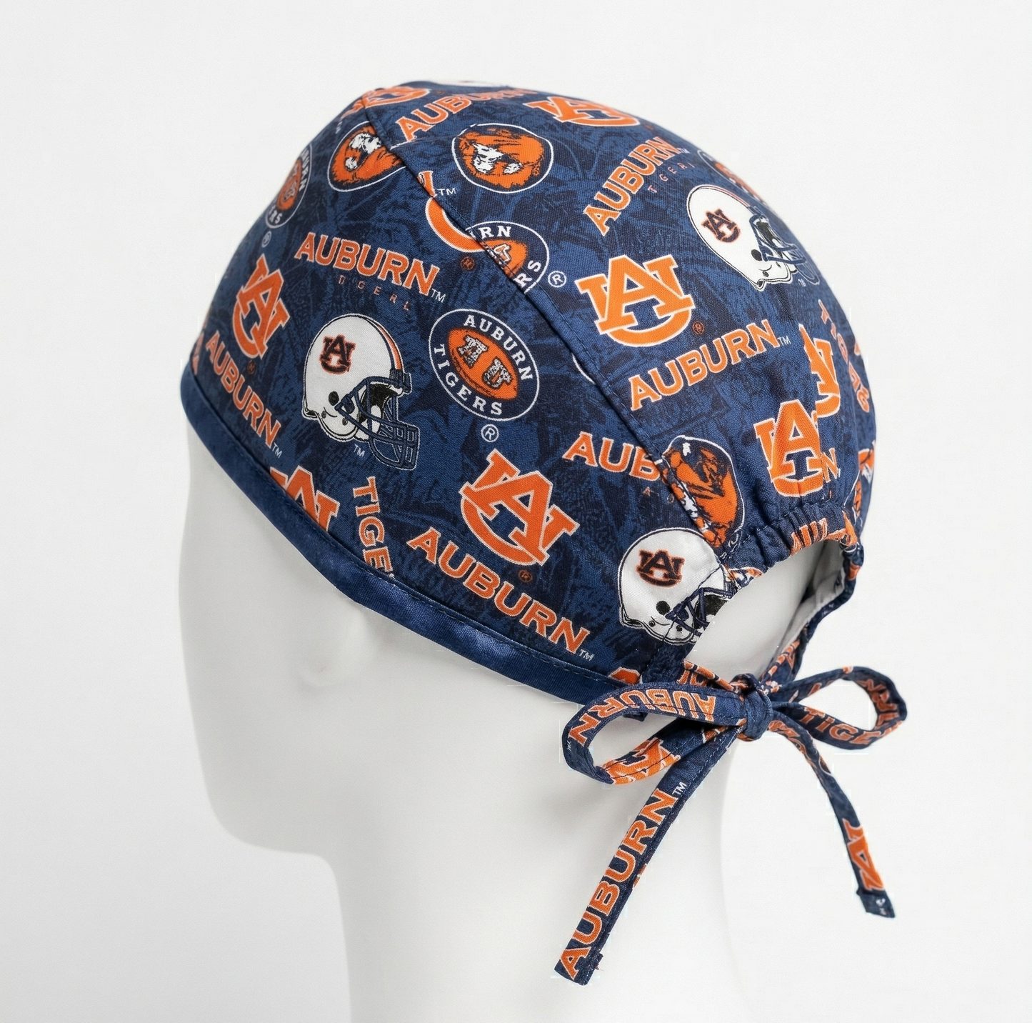 Side profile view of an Auburn Tigers surgical cap on a white mannequin head, featuring the orange and blue "AU" logo on a navy blue background with adjustable tie-backs.