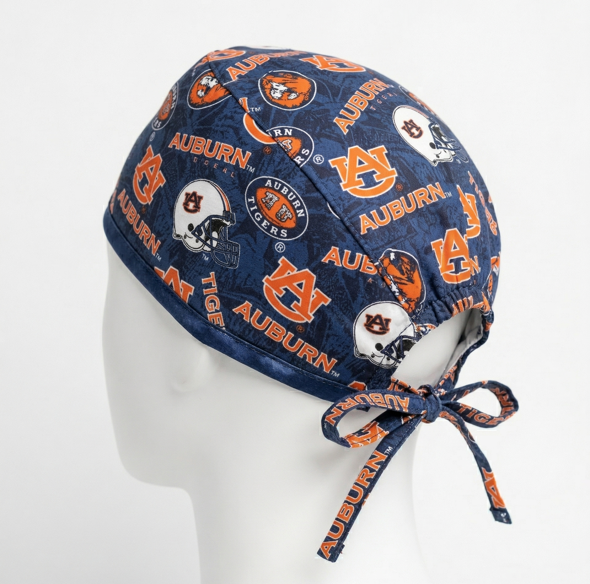 Side profile view of an Auburn Tigers surgical cap on a white mannequin head, featuring the orange and blue "AU" logo on a navy blue background with adjustable tie-backs.