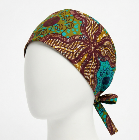 Bronze & Turquoise Surgical Cap 1: A studio product photograph of a tie-back surgical cap featuring a complex bronze, turquoise, and maroon geometric pattern. It is shown on a white mannequin head against a plain white background, highlighting the adjustable ties at the back.