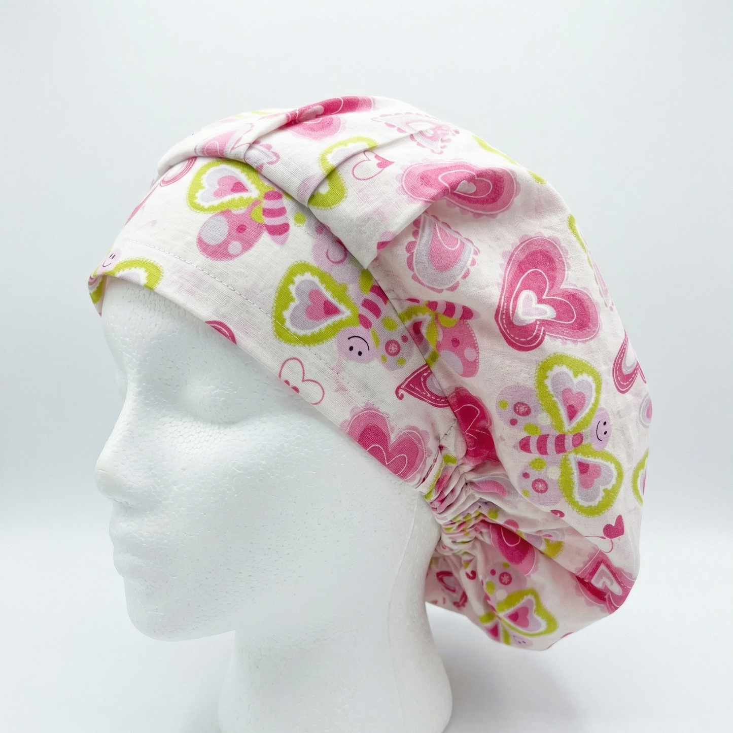 Side profile of a white mannequin head wearing a teal scrub cap with a pink and white butterfly and heart pattern.