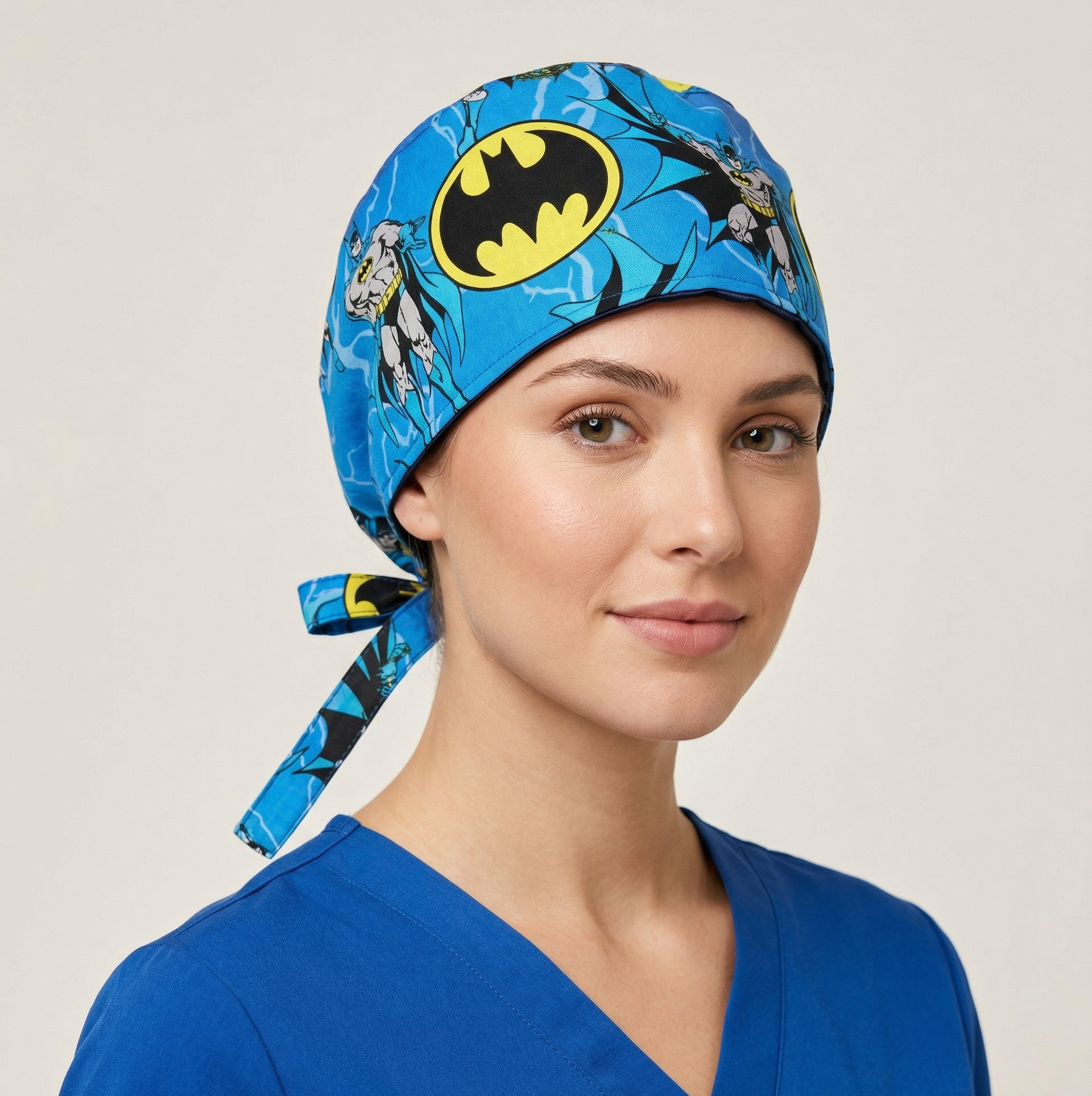 A female model wearing the blue Batman themed surgical cap against a neutral studio background, demonstrating a secure and comfortable fit.
