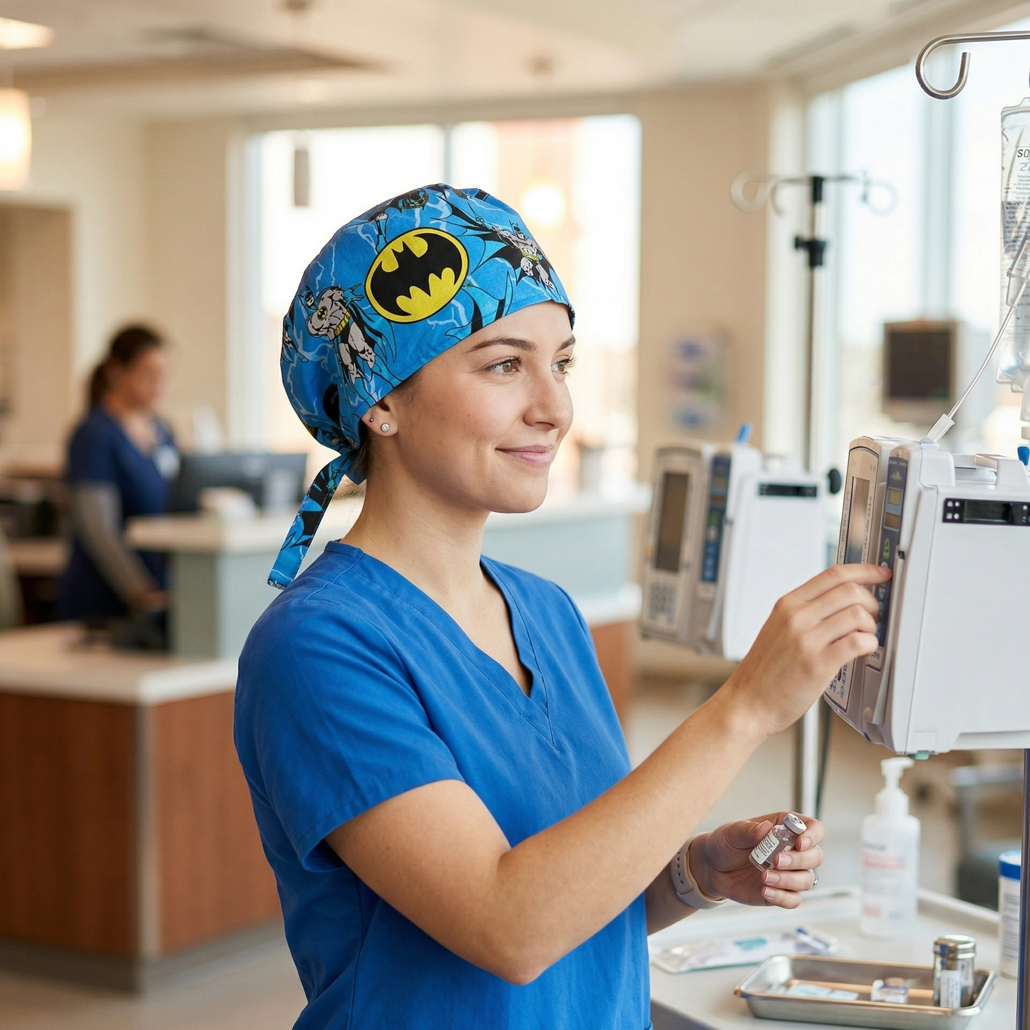 A healthcare professional in blue scrubs wearing the Batman surgical cap while working in a bright, modern clinical environment.