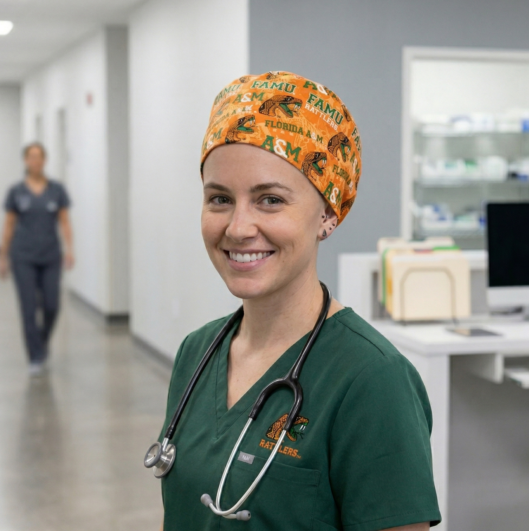 FAMU Florida A&M Rattlers Surgical Cap 3: A lifestyle image of a female medical professional standing in a hospital hallway. She is wearing the dark green scrubs and the orange Florida A&M Rattlers surgical cap, looking toward the camera.