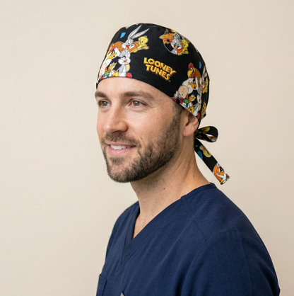 A healthcare professional in a medical office, shown in profile wearing the butterfly and hearts patterned scrub cap while looking at a laptop.