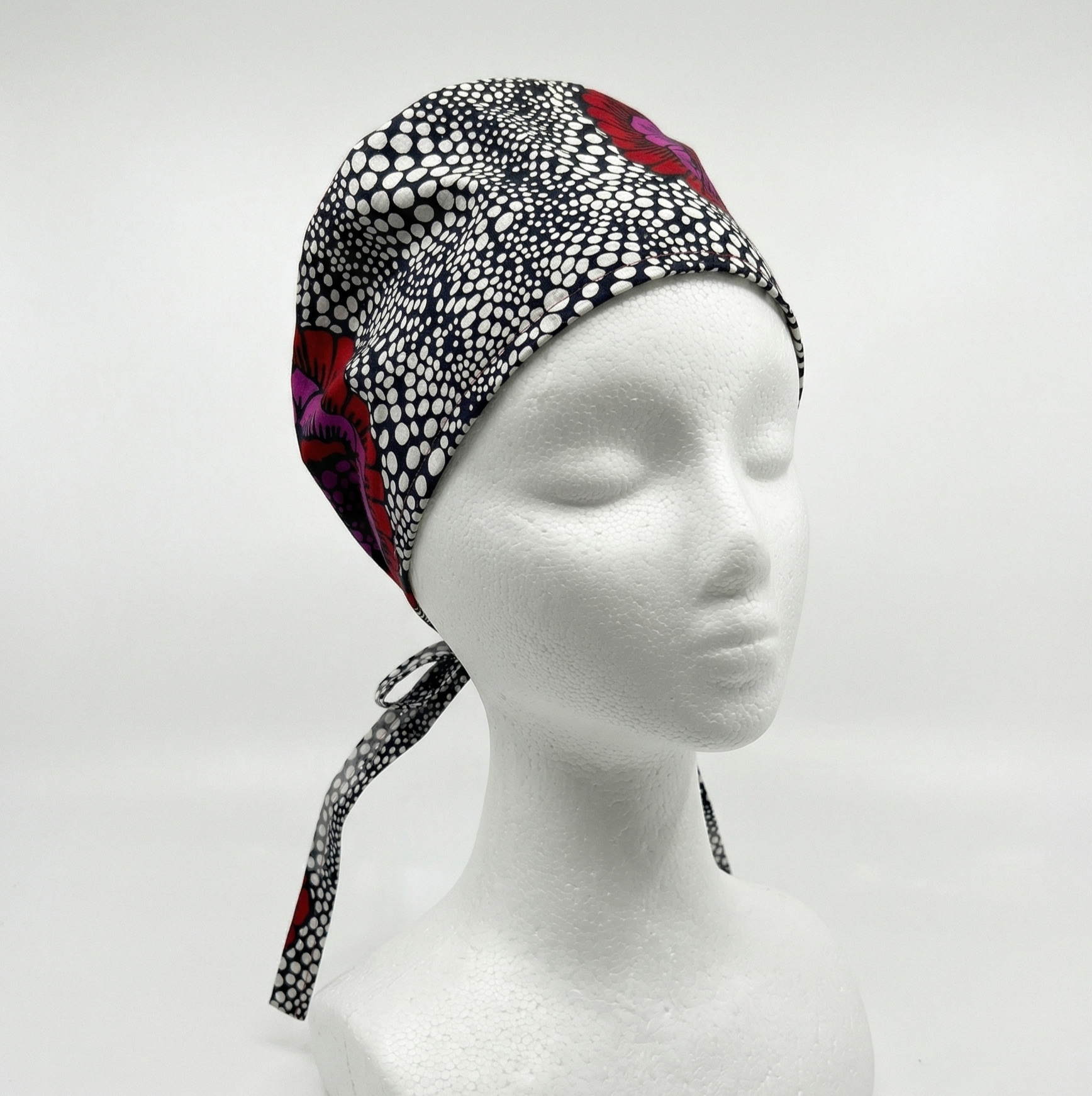 Modern Black Bubbles & Flower Surgical Cap 1: A studio product shot of a patterned surgical cap displayed on a white mannequin head against a clean, neutral background. The cap features a black and white geometric bubble pattern with a prominent red flower accent on the side.