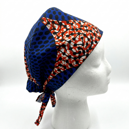 Vibrant Circle Ankara African Print Surgical Cap 1: A studio product photograph of a surgical cap on a white mannequin head. The cap features a bold Ankara print with a deep blue circular pattern contrasted against a vibrant orange and white geometric section.